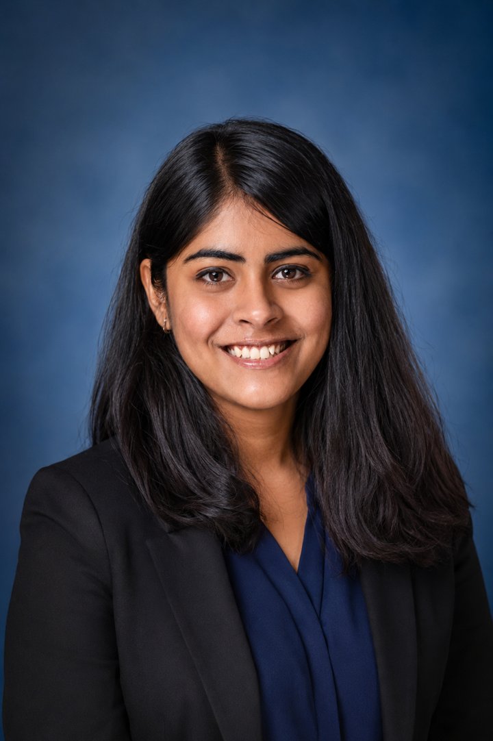 Asmita Saha smiling in a dark blazer against a blue background